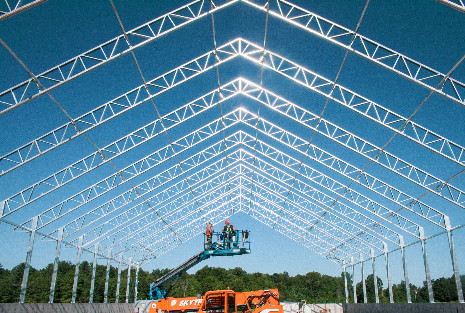 Steel trusses being erected during fabric building construction with boom lift